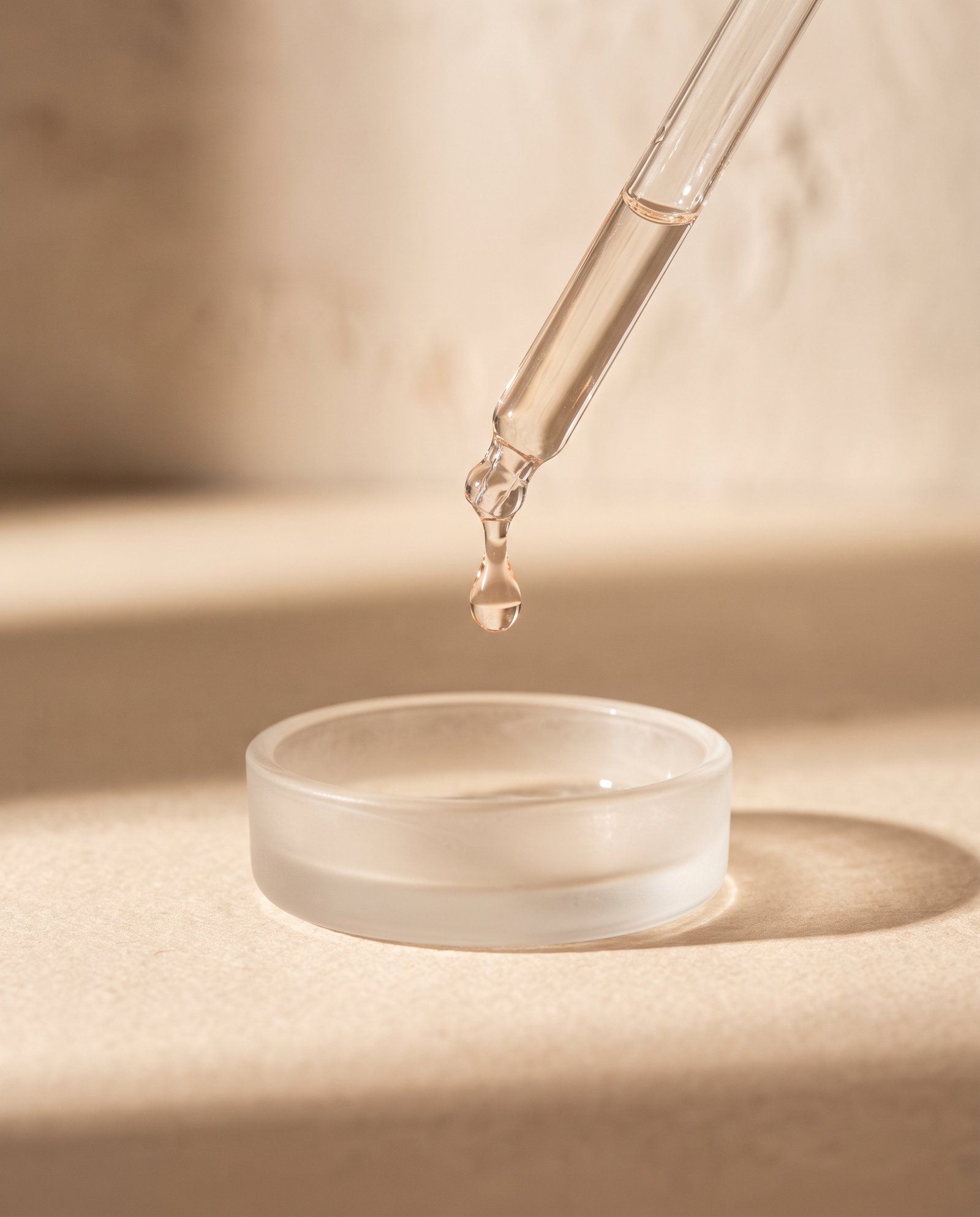 A glass pipette above a dish, a single droplet caught mid-fall.